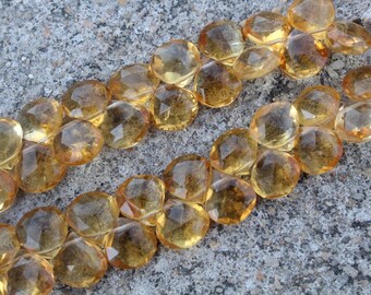 May include: Close-up of two strands of faceted, golden-yellow citrine gemstone beads. The beads are oval-shaped and have a sparkling, translucent appearance. The background is a rough, gray stone surface.