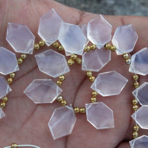 Puede incluir: Un collar de cuentas de piedras preciosas facetadas de color rosa pálido con forma geométrica. Las cuentas están ensartadas con pequeñas cuentas de color dorado. Las piedras preciosas se sostienen en una mano.