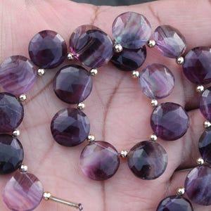 Könnte beinhalten: Eine Halskette aus facettierten, runden, violetten Perlen mit silberfarbenen Abstandshaltern. Die Perlen haben verschiedene Violetttöne und sind aufgefädelt. Die Halskette wird auf einer Hand präsentiert.