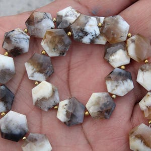 Puede incluir: Un collar de cuentas hexagonales facetadas. Las cuentas son una mezcla de blanco, marrón y gris, con espaciadores dorados. Las piedras preciosas tienen un aspecto natural veteado y están ensartadas.