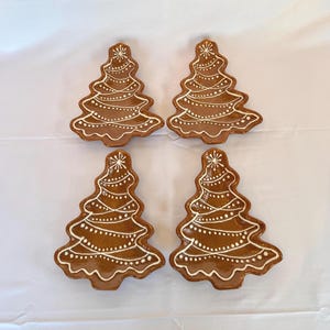 Puede incluir: Cuatro platos marrones de cerámica con forma de árbol de Navidad con detalles de glaseado blanco. Cada plato tiene un borde festoneado y está decorado con puntos blancos y una estrella en la parte superior. Los platos están colocados sobre una superficie blanca.