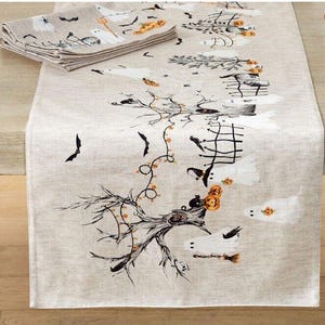 May include: A beige linen table runner with a Halloween theme. The runner features a black and white illustration of a spooky tree with ghosts, bats, and pumpkins.