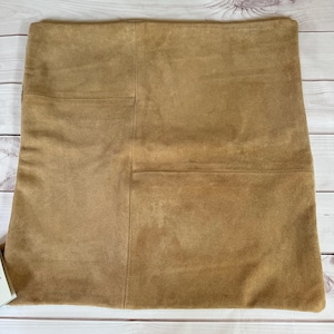 May include: A tan suede pillow cover with a stitched design. The pillow cover is made of soft, textured fabric.