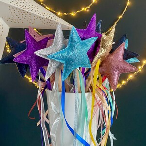 May include: A bunch of colourful star-shaped wands with glittery fabric and wooden sticks. Each wand has a different coloured ribbon attached to the end.