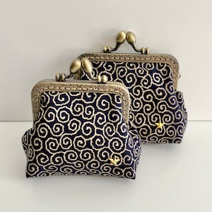 Peut inclure: Deux porte-monnaie noirs avec des cadres et des fermoirs en métal doré. Les porte-monnaie sont décorés d'un motif en spirale et d'une étoile dorée.