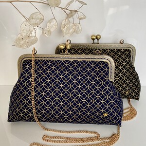 May include: Two gold-toned clasp purses with a chain strap. The purse on the left has a navy blue fabric with a gold geometric pattern. The purse on the right has a black fabric with a gold geometric pattern.