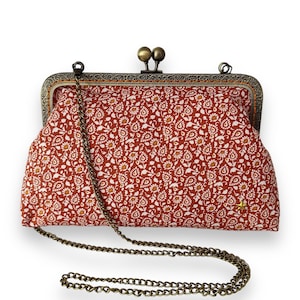 Puede incluir: Un bolso de mano con estampado floral rojo y blanco con un marco y una cadena de metal bronce. El cierre presenta dos pequeños acentos redondos de bronce. El bolso es de estilo clásico, adecuado para llevar lo esencial.