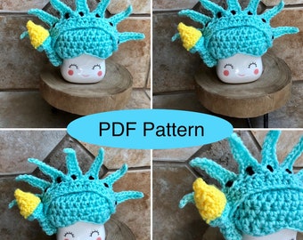 May include: Crochet pattern for a Statue of Liberty mug cozy. The cozy is blue with yellow accents and black details. The pattern is available as a PDF download.