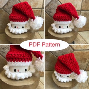 May include: Four crocheted Santa mug toppers in red and white. Each topper features a Santa hat with a white pom-pom and a white beard. The toppers are displayed on wooden coasters. PDF Pattern.