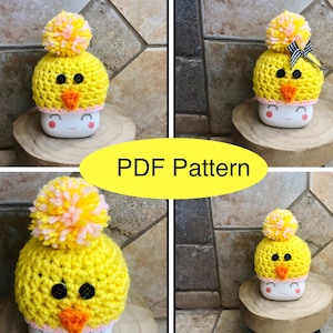 Puede incluir: Cuatro gorros de ganchillo de pollito en amarillo con pompones rosa y blanco. Los gorros están encima de tazas blancas con un diseño de cara sonriente. El texto "PDF Pattern" está en amarillo sobre fondo blanco.