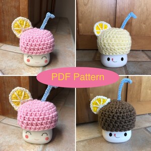 May include: Four crocheted lemon-shaped hats with blue straws on top of white mugs with a smiley face. The hats are pink, yellow, and brown.