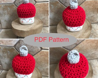 May include: A crochet mug cozy in the shape of a mushroom with a red top and a gray top. The cozy is on a white mug with a smiling face.