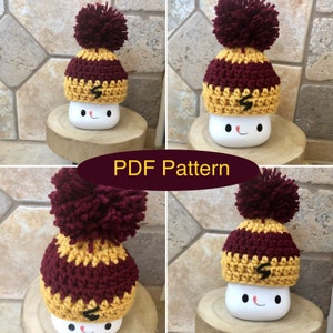 May include: Four crocheted hats in maroon and gold with a pom-pom on top. The hats are sitting on top of white ceramic mugs with a smiling face.
