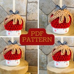 May include: Four crocheted mug cozies in the shape of caramel apples. Each cozy is red with a brown crocheted caramel topping and a black and white bow. The cozies are sitting on a wooden surface. PDF PATTERN.