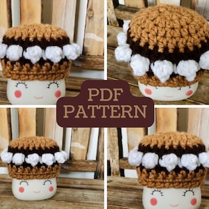 May include: Crochet mug cosy pattern in the shape of a s'more. The cosy is brown with a brown chocolate layer and white marshmallow topping. The pattern is available as a PDF download.