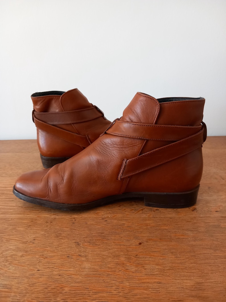 May include: A pair of brown leather ankle boots. The boots feature a pointed toe, a low heel, and a strap detail around the ankle. The leather has a slightly worn appearance.