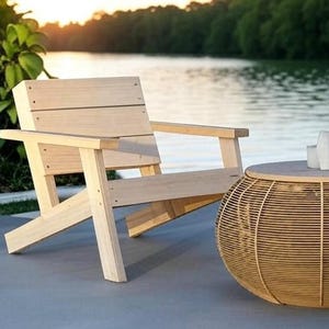 Op de afbeelding: Een houten stoel met een natuurlijke afwerking staat naast een ronde rieten bijzettafel met een houten blad. De stoel en de tafel staan op een grijs betonnen terras.
