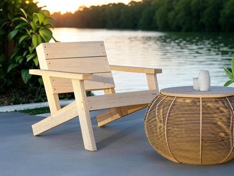 Op de afbeelding: Een houten stoel met een natuurlijke afwerking staat naast een ronde rieten bijzettafel met een houten blad. De stoel en de tafel staan op een grijs betonnen terras.