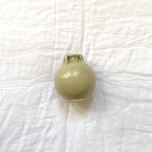 May include: A small, round, celadon-coloured ceramic vase with a crackle glaze. The vase has a bulbous body and two small handles near the top. The vase is a decorative item.