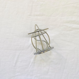 May include: A silver-toned metal wire sculpture featuring a circular frame with an intersecting triangular structure and a horizontal bar across the top. The object has a polished, reflective finish and is constructed from thin, smooth metal rods.