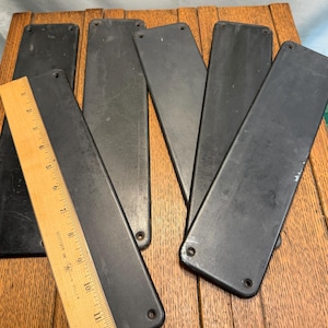 May include: Five rectangular black swing seats made of flexible material, each featuring rounded corners and two pre-drilled holes at the top and bottom. A wooden ruler is placed over one seat, showing a length of approximately 12 inches.