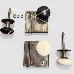 May include: Two metal door plates with round knobs, one black and one white, plus a separate white knob on a metal spindle. The black knob and plate assembly is marked with a white X and the text Sold, indicating it is no longer available.