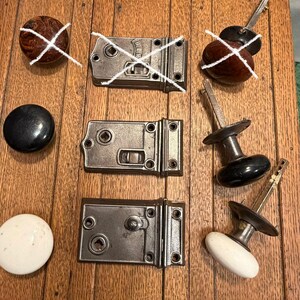 May include: A collection of two metal rim locks and two matching door knobs in black and white. The locks feature rectangular plates with screw holes and a central square spindle opening. The knobs are round with metal stems and spindles.