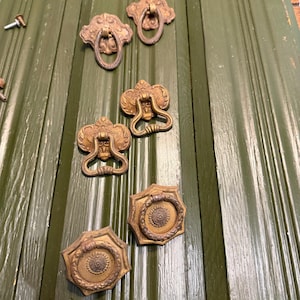 May include: Antique brass drawer pulls and handles in various ornate designs. The hardware is set against a green painted wooden surface. Includes screws for installation. Ideal for vintage furniture restoration projects.