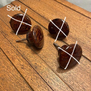 May include: Four vintage brown cabinet knobs with a marbled pattern. The knobs are round with a stem for mounting. The word "Sold" is written in white across the top left knob.