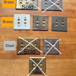 May include: A collection of rectangular metal light switch plates with various finishes including brass and steel. Some plates feature four circular openings for switches, while others have two. Several plates are marked with the text Sold.