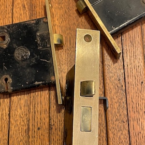 May include: Close-up of antique door locks. The locks are made of brass and black metal. The brass locks have a shiny finish, while the black locks show signs of wear. The locks are arranged on a wooden surface.