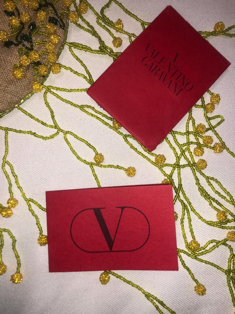 May include: Two red cards featuring the Valentino Garavani logo. One card displays the full brand name, while the other showcases the letter V within a circle.