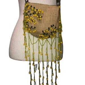 May include: A brown burlap crossbody bag with yellow and green beaded fringe. The bag features a floral design with yellow beads and black accents.