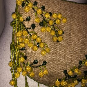 May include: A small, brown, beaded purse with a fringe of green and yellow beads. The purse is decorated with a floral design of yellow and green beads.