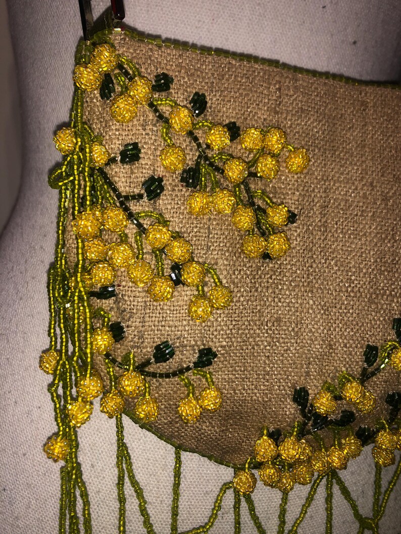 May include: A small, brown, beaded purse with a fringe of green and yellow beads. The purse is decorated with a floral design of yellow and green beads.