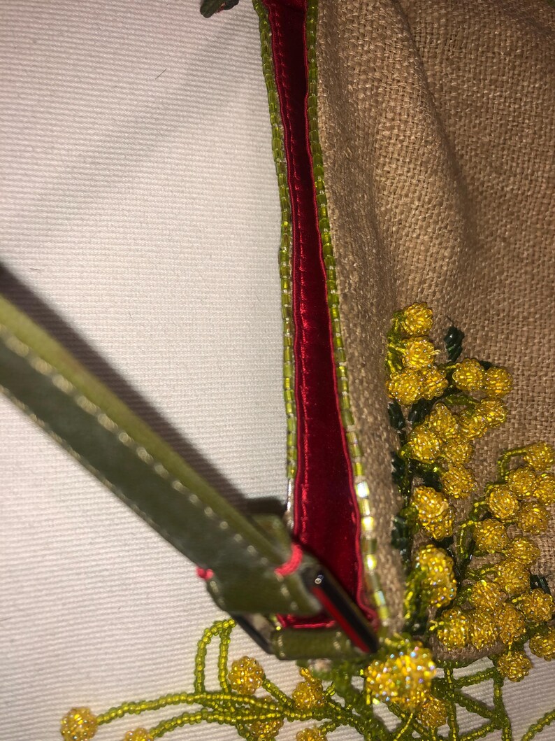 May include: A small, brown, burlap handbag with a red velvet trim and a green beaded strap. The bag is decorated with yellow and green beaded flowers.