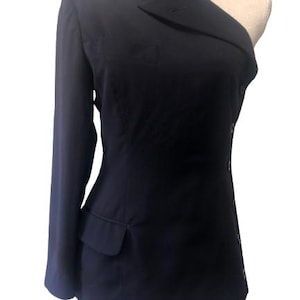 May include: A navy blue one-shoulder blazer with a single long sleeve. The blazer features a notched lapel, a single-button closure, and a pocket on the front. The garment is displayed on a mannequin.