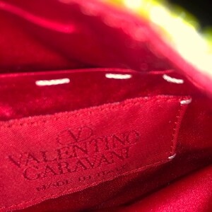 May include: Close-up of a red fabric label with white stitching. The label reads "VALENTINO GARAVANI" in white lettering and "MADE IN ITALY" in smaller white lettering.