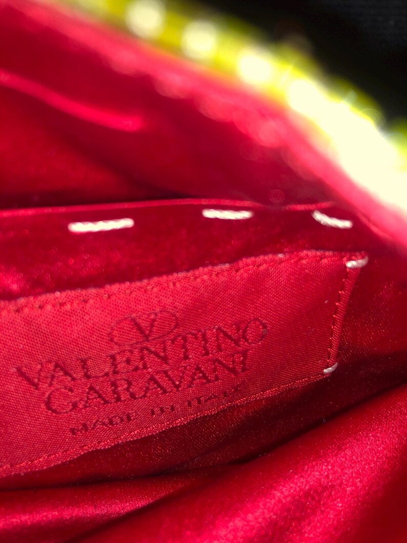 May include: Close-up of a red fabric label with white stitching. The label reads "VALENTINO GARAVANI" in white lettering and "MADE IN ITALY" in smaller white lettering.
