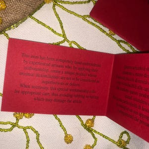 May include: A red card with white text explaining that the item is hand-embroidered and requires special care to avoid damage. The text reads: "This item has been completely hand-embroidered by experienced artisans who, by applying their craftsmanship, create a unique product whose minimal dissimilarities are not to be considered as imperfections or defects. When necessary, this special workmanship calls for appropriate care, thus avoiding rubbing or hitting which may damage the article."