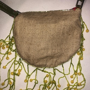 May include: A small, brown, burlap handbag with a green leather strap and a fringe of green and yellow beads.