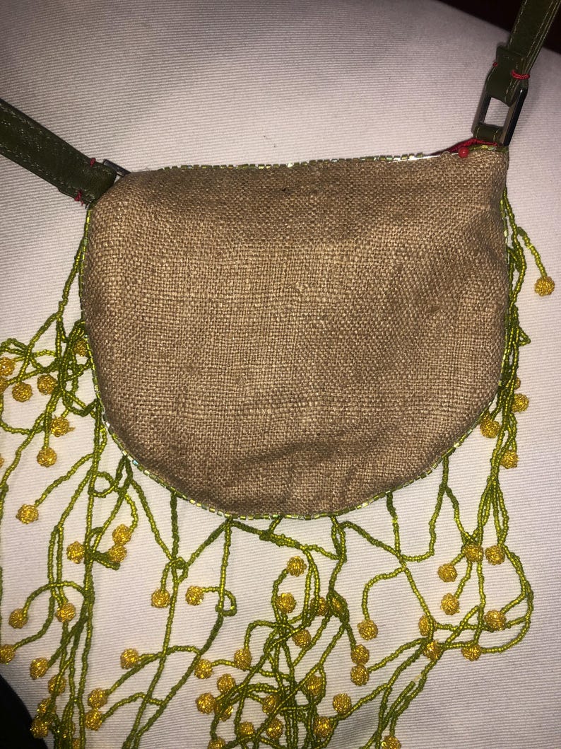 May include: A small, brown, burlap handbag with a green leather strap and a fringe of green and yellow beads.