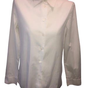 Può includere: Una camicia bianca a maniche lunghe con un classico colletto a punta, un'abbottonatura frontale a tutta lunghezza con bottoni bianchi abbinati e polsini strutturati all'estremità di ogni manica, presentata in un design pulito e semplice.