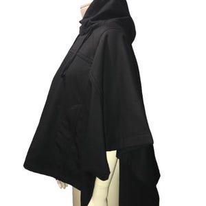 Può includere: Poncho nero con cappuccio e design lungo e fluido. Il poncho ha un cappuccio grande e una coda lunga e fluida.
