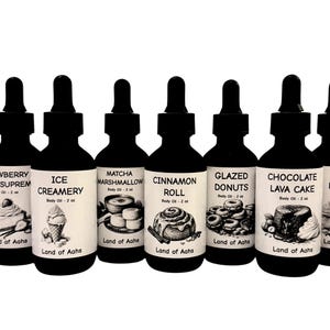 Puede incluir: Una colecci&oacute;n de botellas cuentagotas negras, cada una etiquetada con un aroma diferente con tem&aacute;tica de postre. Las etiquetas presentan ilustraciones de helado, rollos de canela y pastel de lava. Cada botella contiene 60 ml de aceite corporal y es de "Land of Aahs".