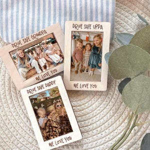 May include: Three wooden photo frames with family photos. Each frame has the words "DRIVE SAFE" followed by "GRANDPA", "UPPA", or "DADDY" at the top. The phrase "WE LOVE YOU" is at the bottom of each frame. The frames are on a textured surface.