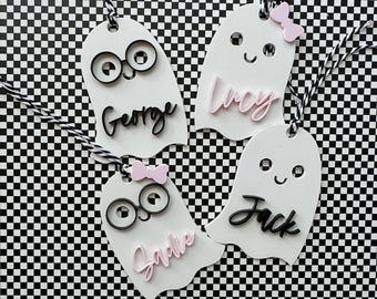May include: Four white ghost-shaped gift tags with black eyes and mouths. Each tag has a different name written on it: George, Lucy, Jack, and Sadie. The tags are decorated with pink bows.