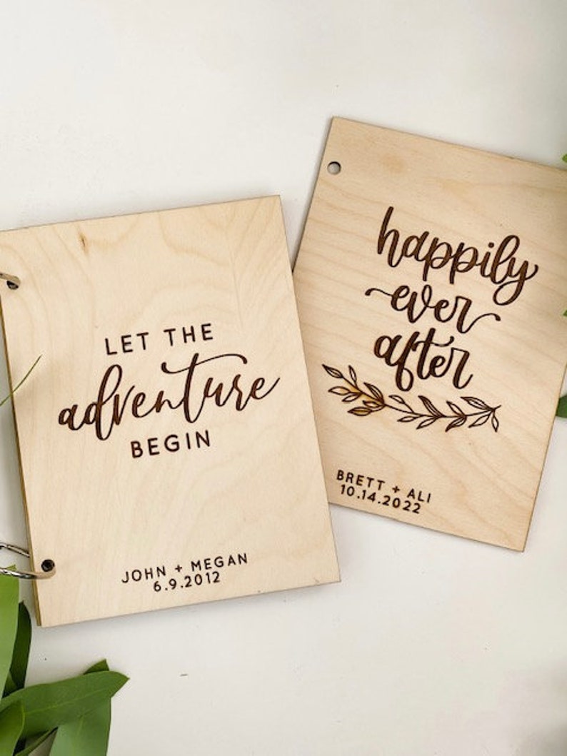 K&ouml;nnte beinhalten: Zwei Holzschilder mit eingraviertem Text. Das erste Schild sagt "Let the adventure begin" mit dem Datum "6.9.2012" und den Namen "John + Megan". Das zweite Schild sagt "happily ever after" mit dem Datum "10.14.2022" und den Namen "Brett + Ali".