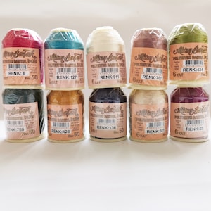 May include: A collection of ten spools of thread in various colors, including red, green, blue, gold, and beige. Each spool is labeled with the brand name "Mizan Batik" and a color code, such as "RENK: 6" and "RENK: 127".