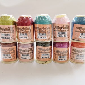 May include: Ten spools of thread in various colors, including green, red, blue, pink, brown, purple, and orange. Each spool is labeled "Altin Bayrak" and has a color code and number. The thread is for sewing and crafting.